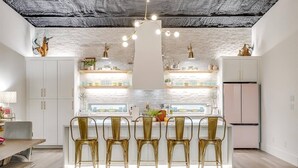 Une cuisine moderne avec des meubles blancs, un îlot central doté de tabourets de bar et un plafond au style rustique.