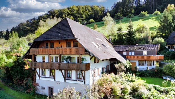 Een chalet met twee verdiepingen en een balkon, omringd door weelderig groen en een glooiend landschap.