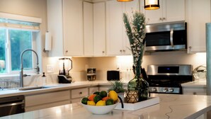 A modern kitchen with white cabinets, a marble countertop, a bowl of fruit, and decorative plants. - Charming Spacious Riverside 2-bedroom house in welcoming Reno with AC, WiFi (Reno)