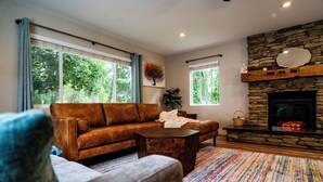 A cozy living room with a stone fireplace, a brown leather sofa, and a colorful striped rug. - Charming Spacious Riverside 2-bedroom house in welcoming Reno with AC, WiFi (Reno)