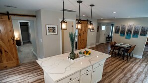 A kitchen with a marble island, wooden flooring, pendant lighting, and a dining area with chairs and a table. - Charming Spacious Riverside 2-bedroom house in welcoming Reno with AC, WiFi (Reno)