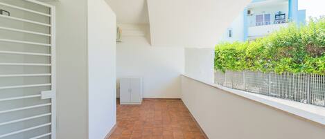 A narrow corridor with a tiled floor, white walls, and a white door with horizontal bars.