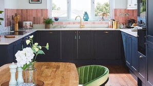 Une cuisine moderne avec des meubles de couleur sombre, une table à manger en bois et une chaise recouverte d’un tissu vert.