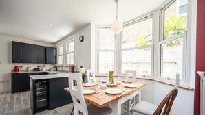 Una cocina moderna con armarios oscuros, una isla central y un comedor con mesa de madera y sillas blancas.
