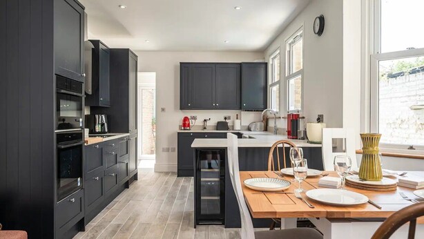 Una cocina moderna con armarios oscuros, una isla central y una zona de comedor con una mesa y sillas de madera.