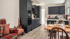 Una cocina moderna con armarios oscuros, un comedor con mesa de madera y una zona de estar acogedora con un sofá a cuadros.