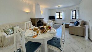 Una sala de estar con chimenea, una mesa de comedor con desayuno, dos sofás y un televisor.