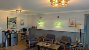 A living room with two sofas, a coffee table, a small table with a lamp, and a kitchen area with appliances. - The Candlelight Inn (Rocky Harbour)