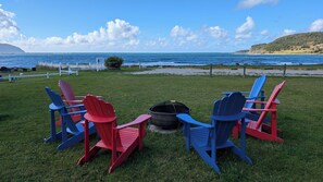 A grassy area with Adirondack chairs and a fire pit, overlooking a coastal view. - The Candlelight Inn (Rocky Harbour)