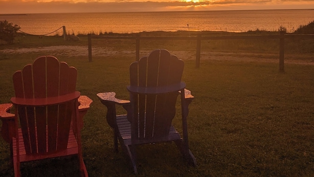 Two Adirondack chairs facing a sunset over a beach. - The Candlelight Inn (Rocky Harbour)
