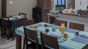 A dining area with wooden tables and chairs, a hexagonal skylight, a clock, and a kitchen area with cabinets. - The Candlelight Inn (Rocky Harbour)