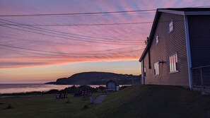 A coastal house with a view of the ocean at sunset. - The Candlelight Inn (Rocky Harbour)