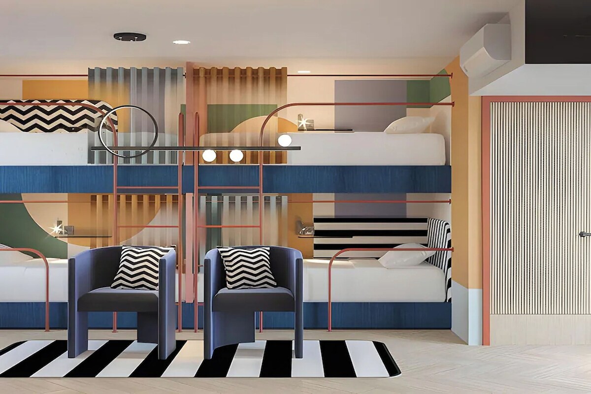 A multi-level bunk bed room with a striped rug, two armchairs with striped pillows, and a modern ceiling design.
