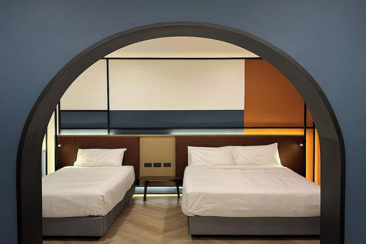 A hotel room with two beds, a wooden headboard, and a large arched window.