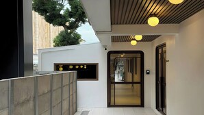 A modern hallway with a glass door entrance, a concrete barrier, and a ceiling with recessed lighting. - Parcel Hotel Bangkok (Bangkok)