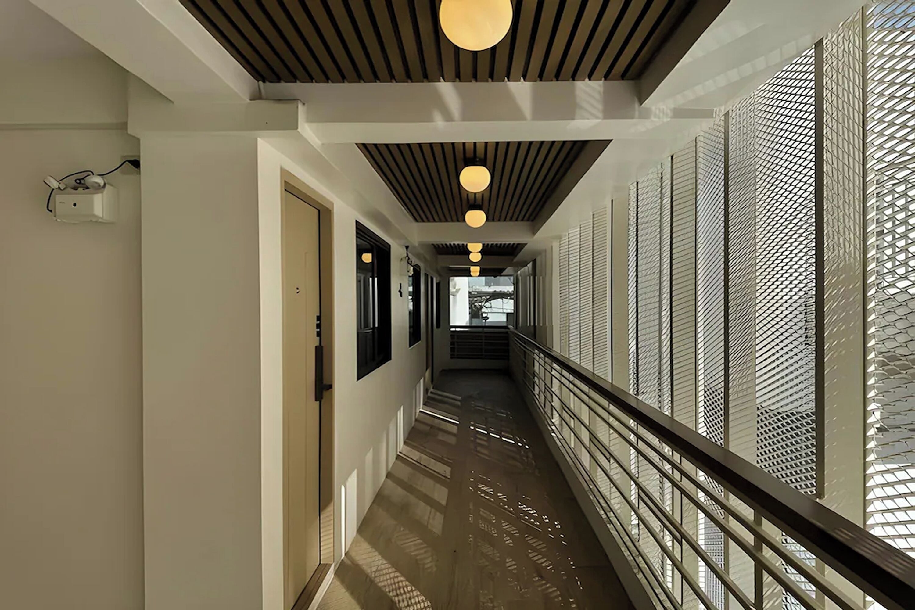Un pasillo moderno de hotel con techo de madera, luces colgantes y un panel metálico con diseño.