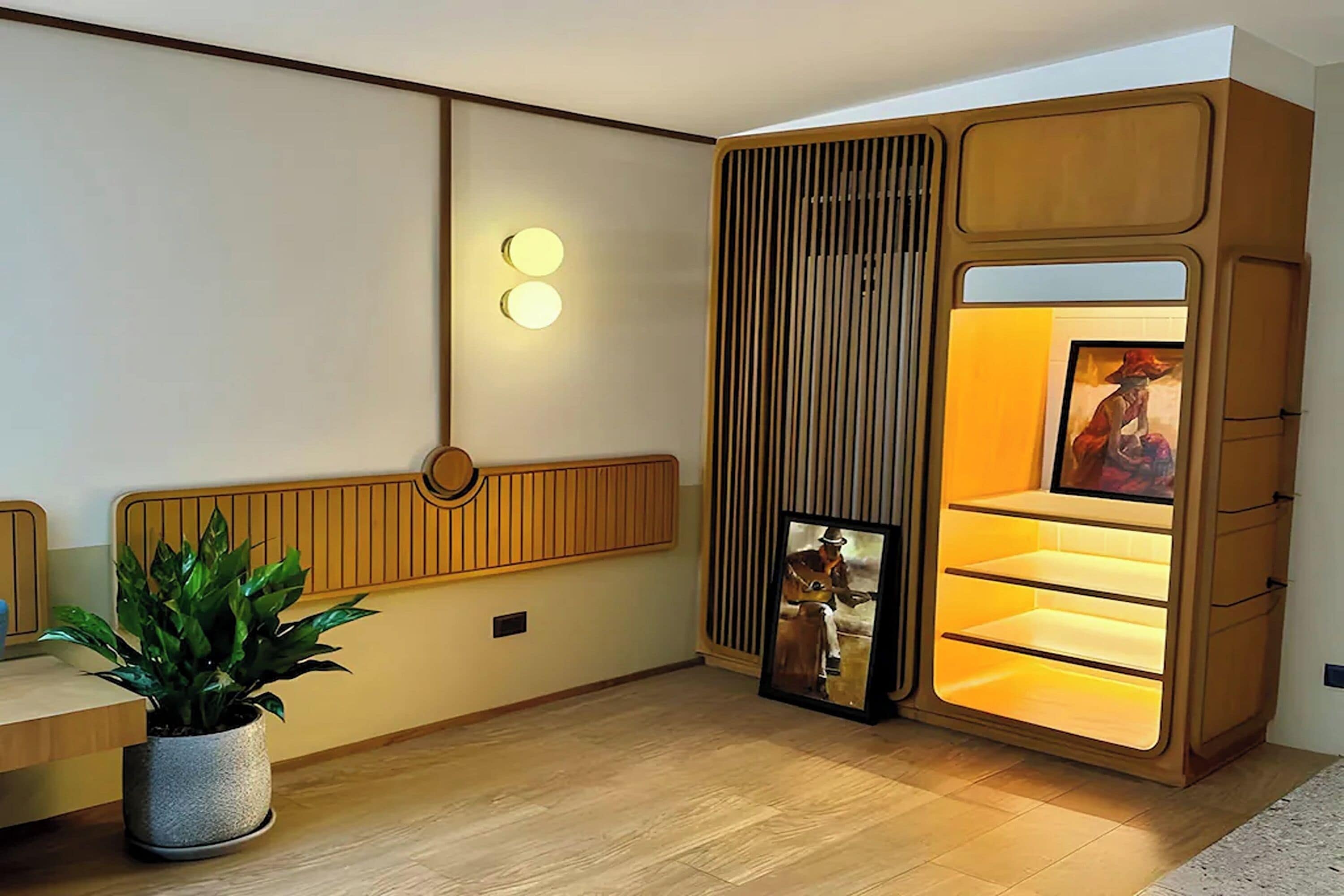 Un intérieur moderne avec un mur lambrissé en bois, une plante en pot et une bibliothèque intégrée agrémentée d’un tableau encadré.