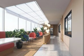 A modern indoor space with a long corridor, seating areas with red and blue chairs, potted plants, and a white reception desk. - Parcel Hotel Bangkok (Bangkok)