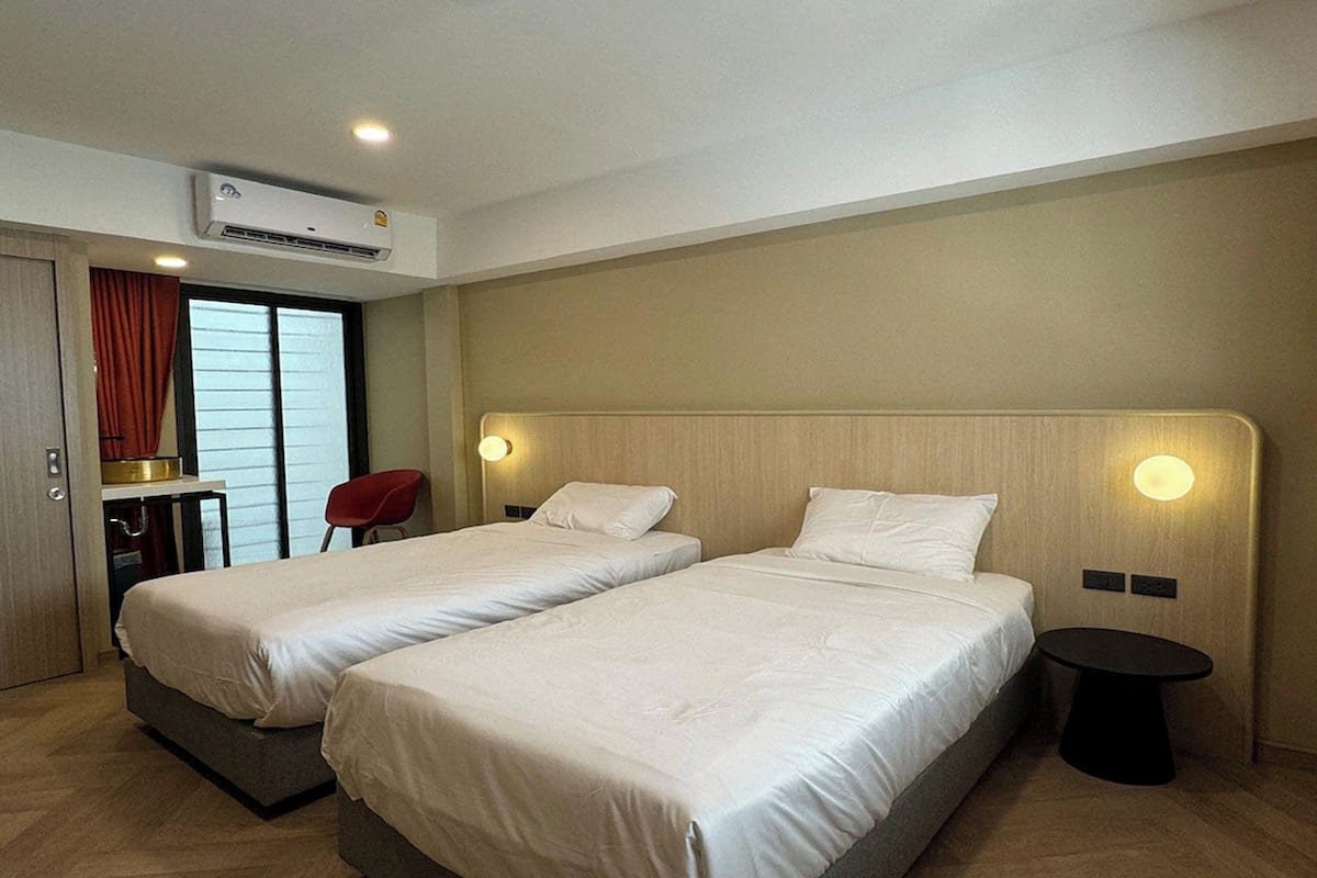 A hotel room with two beds, a desk, a chair, and an air conditioning unit.
