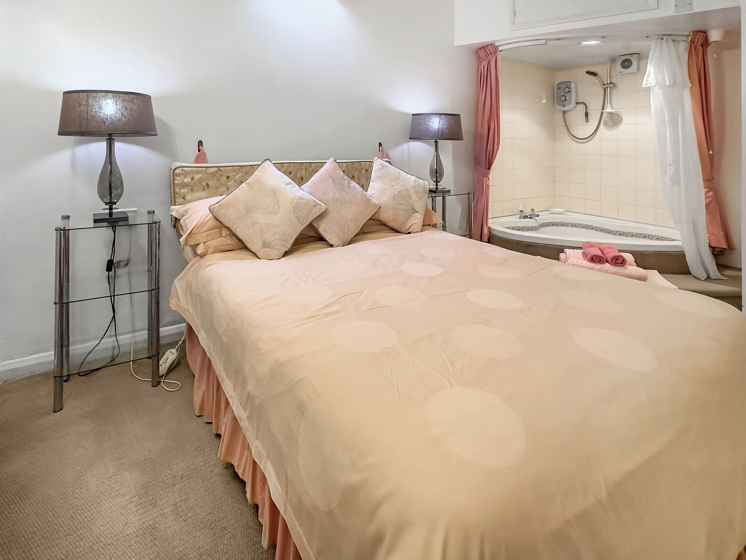 A bedroom with a bed, two bedside lamps, a bedside table, a bathroom with a bathtub, and a shower.