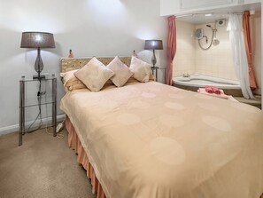 Un dormitorio con cama, dos lámparas de noche, mesita de noche y un baño con bañera y ducha.