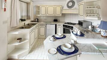 Une cuisine moderne avec des meubles blancs, un plan de travail en marbre et un coin repas où sont disposées des assiettes et des tasses.