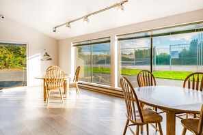 A spacious room with large windows, a round table, and wooden chairs.