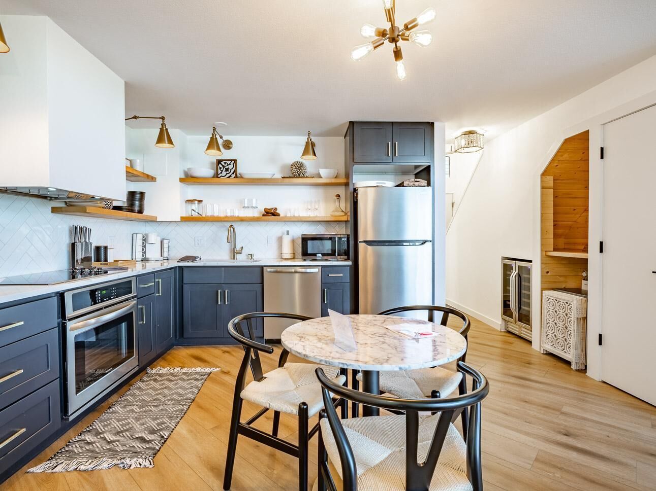 Una cocina moderna con armarios oscuros, electrodomésticos de acero inoxidable y una mesa redonda de mármol con cuatro sillas.