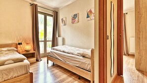 Une pièce comprenant un lit, une table de chevet avec une lampe, une fenêtre avec des rideaux et une porte donnant sur une autre pièce.