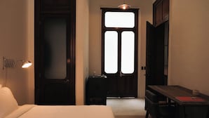 Ein Hotelzimmer mit Bett, Schreibtisch, Stuhl, einem kleinen Tisch und einer Tür mit Milchglasfenster.