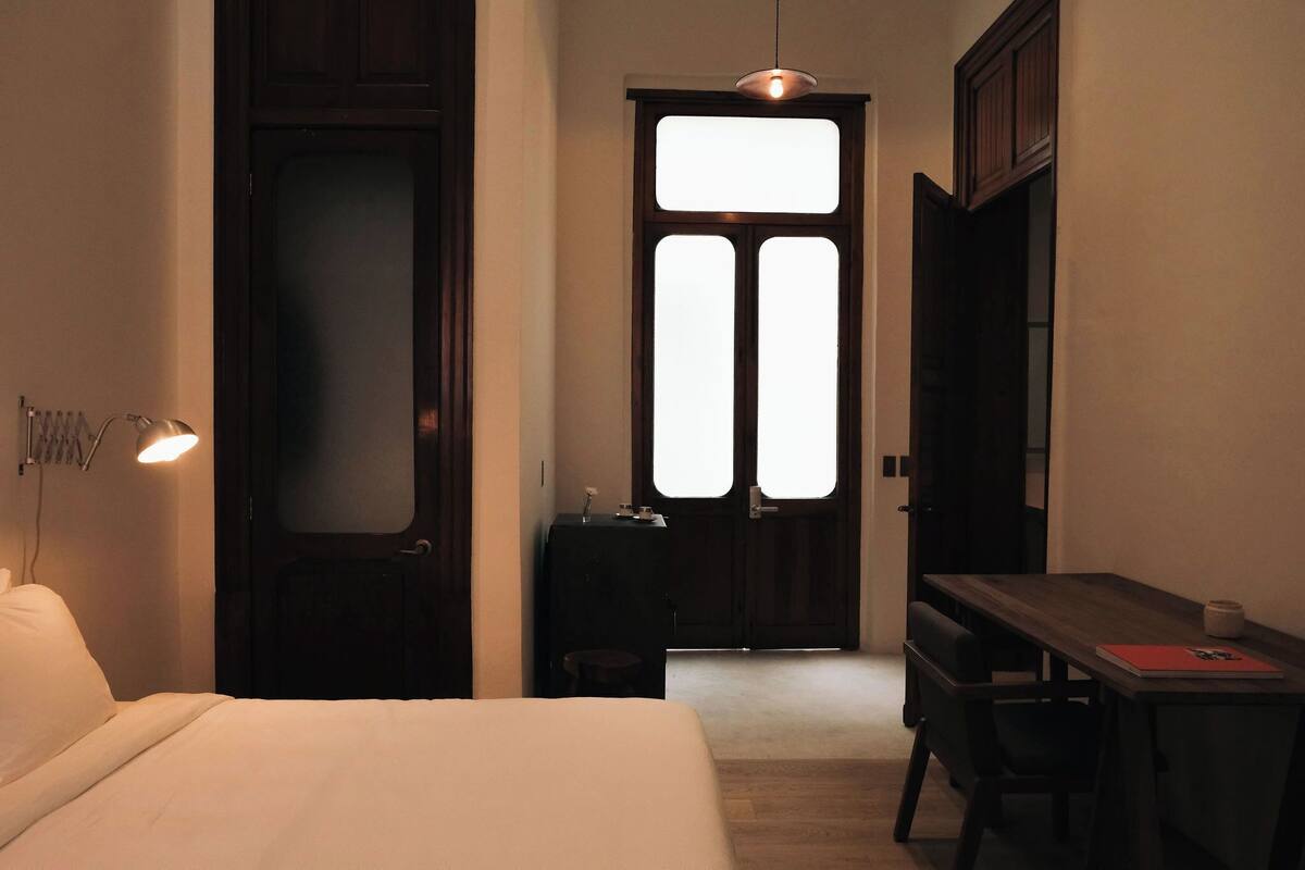 Hotelkamer met een bed, bureau, stoel, klein tafeltje en een deur met een geëtste glazen ruit.