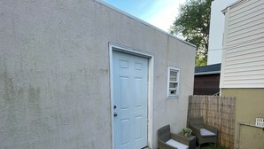 Une petite maison avec une porte blanche, une petite fenêtre et une clôture en bambou.