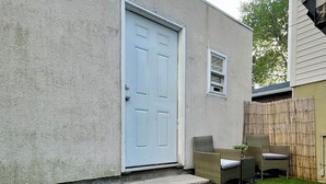 Une maison avec une porte blanche, une petite fenêtre et un porche en béton donnant sur une cour verdoyante.