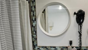 Une salle de bain avec un rideau de douche à rayures, un lavabo avec un miroir au-dessus et un sèche-cheveux fixé au mur.