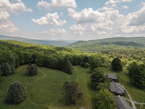 A rural landscape with rolling hills, dense forests, and a few houses with sloped roofs.