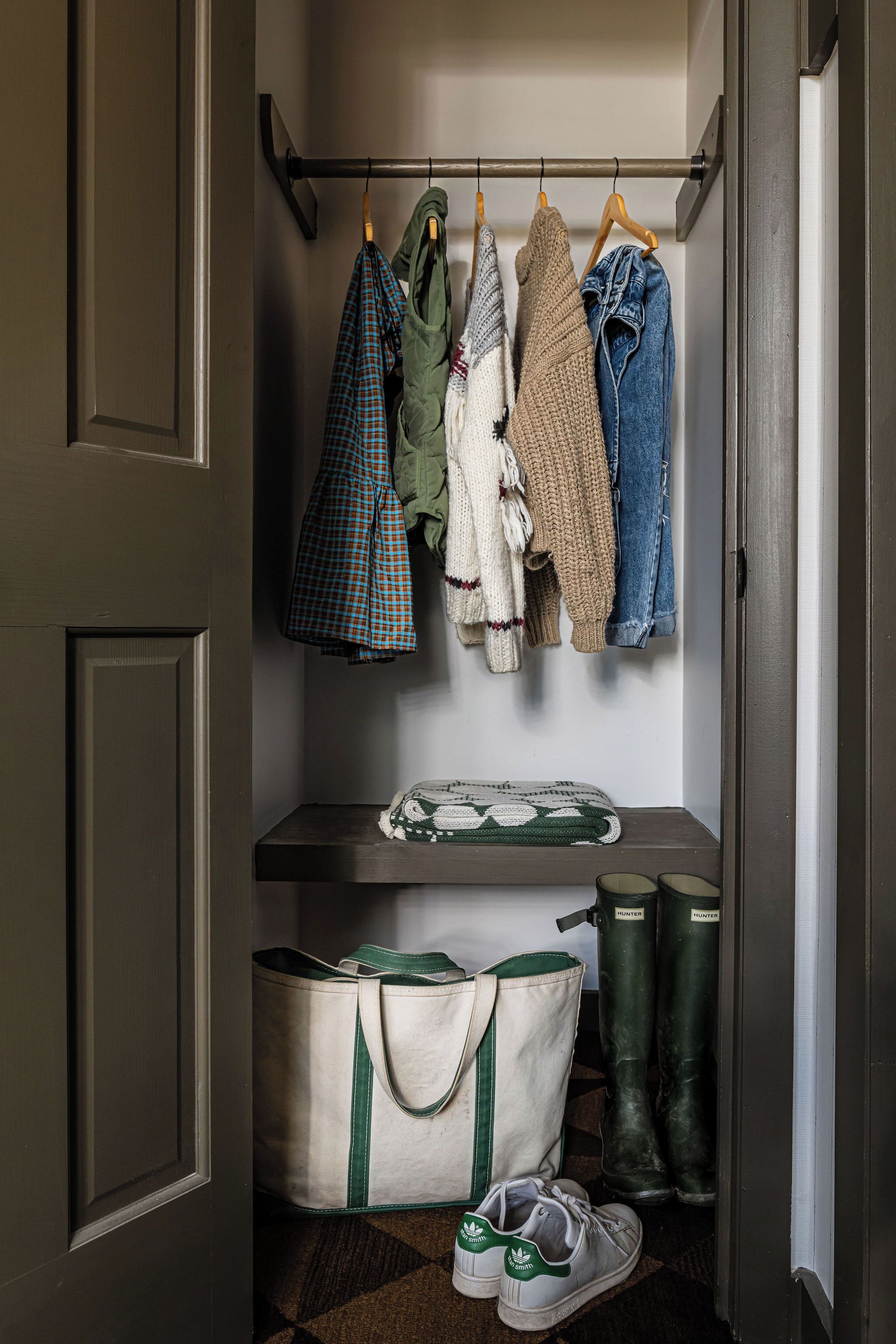 A closet with hanging clothes, a storage bench, a bag, and boots.