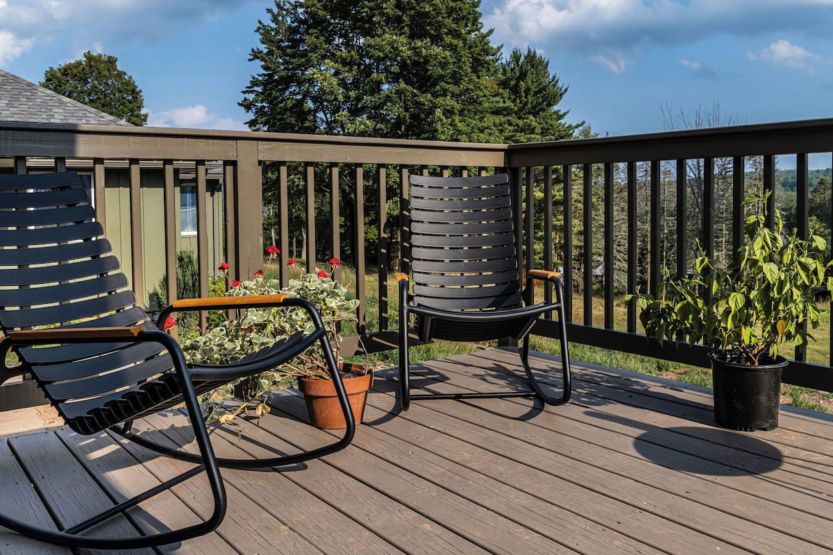 Eine Holzterrasse mit zwei schwarzen Stühlen und einem Blumentopf.