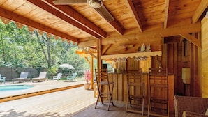 Une terrasse en bois avec une piscine, des chaises longues et un espace salon couvert comprenant des chaises et une table.