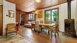 Une pièce au plancher de bois, avec une table et des chaises, un canapé, une cheminée et une grande fenêtre.