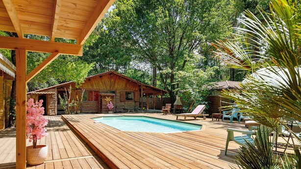 Une terrasse en bois avec une piscine, des chaises longues et un chalet en bois.