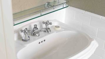 A white pedestal sink with a glass shelf above it, a mirror, and a hexagonal tiled floor.
