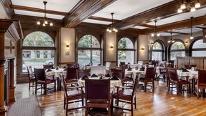 A spacious restaurant with high ceilings, wooden beams, and large arched windows. Tables are set with white tablecloths and red chairs. - Alta Club (Salt Lake City)