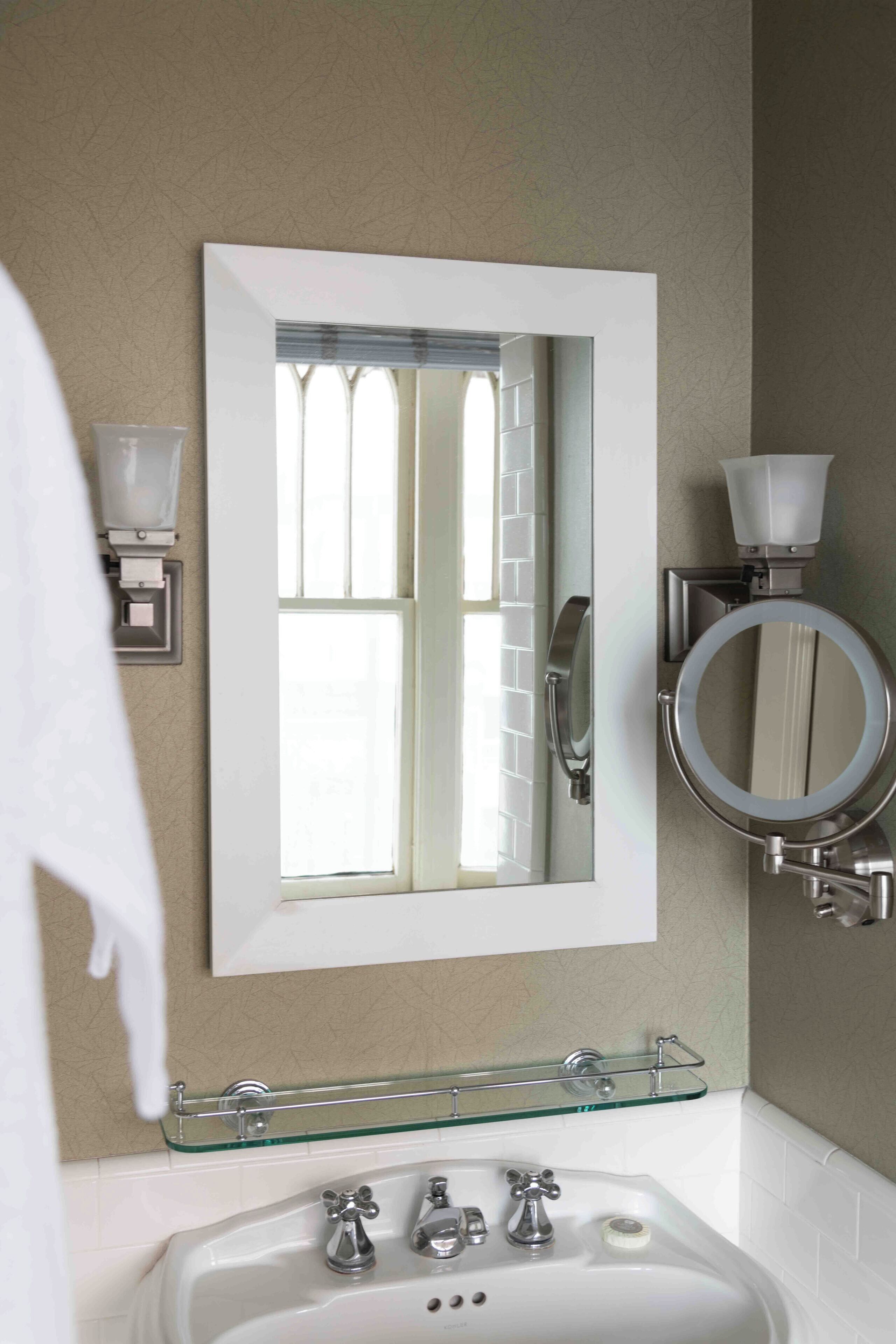Une salle de bain avec un grand miroir, une étagère en verre au-dessus du lavabo et des toilettes dotées d’un miroir rond.