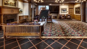 A grand lobby with a fireplace, a large wooden reception desk, a patterned carpet, and a staircase leading to upper floors. - Alta Club (Salt Lake City)