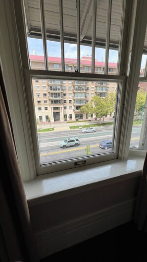 Una ventana con vistas a un edificio de varios pisos con balcones, una calle con coches y un árbol.