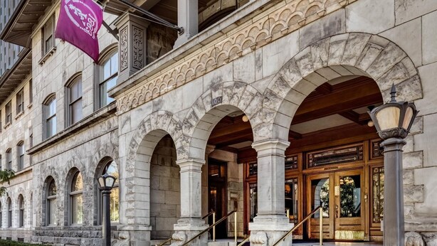 A historic building with stone arches, a grand entrance, and a flag. - Alta Club (Salt Lake City)