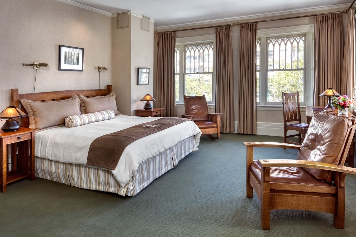 Camera d'albergo con un letto grande, due comodini con lampade, una sedia in legno e vista all'esterno attraverso ampie finestre.