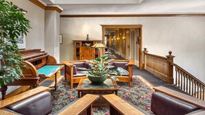 A spacious lobby with a grand piano, wooden furniture, a central table with a plant, and a staircase leading to another area. - Alta Club (Salt Lake City)
