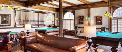 Une salle de billard équipée d’une table de billard, d’un canapé en cuir et de tables en bois.