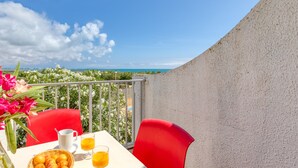 A balcony with a table, red chairs, a wicker basket with fruit, a white mug, and glasses of orange juice. - Studio with Sea View Terrace on the Beach in La Grande Motte – Renovated 2026 (La Grande-Motte)